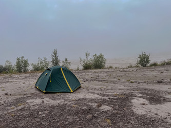Зеленые палатки, разбитые среди редких кустарников на каменистой местности под пасмурным небом - steveee