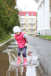 Счастливая маленькая девочка в розовом жилете прыгает в лужу - paha_l