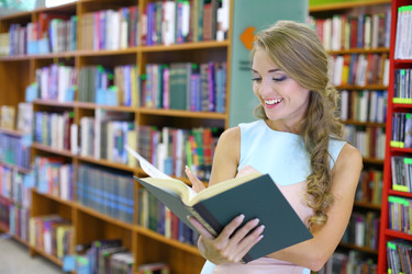 Молодая женщина с радостью рассматривает книгу на книжных полках в библиотеке - paha_l