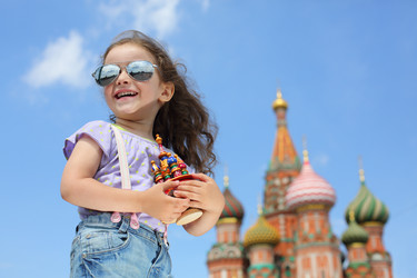 Улыбающаяся маленькая девочка в солнцезащитных очках и джинсах с подтяжками на фоне миниатюрного собора - paha_l