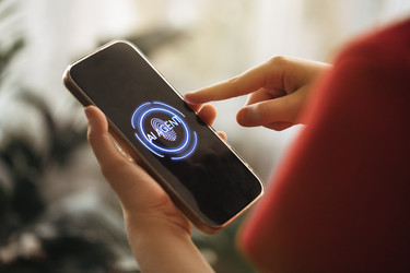 Человек использует смартфон со светящимся экраном, отображающим интерфейс технологии искусственного интеллекта, рука расположена на устройстве, размытый фон с комнатными растениями и мягкое освещение - Darya Petrenko