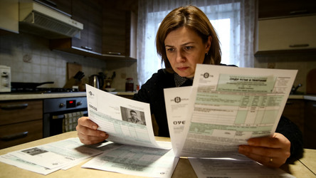 Женщина с тревожным выражением изучает квитанции за коммунальные услуги - Merk011194