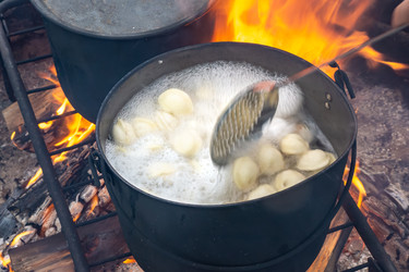 Черный горшок с кипящими пельменями испускает густой пар и насыщенный аромат над открытым пламенем на металлической решетке - dkorostilev78