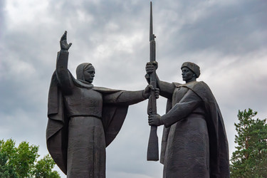 Томск, Россия - 6 июля 2025 года. Рука, благословляющая Родину, встречается с рукой солдата, принимающего в руки винтовку. Бронзовый цвет и пасмурное небо подчеркивают торжественность и символическую значимость межпоколенческого долга. Выборочная фокусиро - dkorostilev78