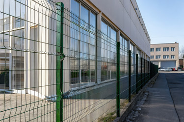 Зеленый сварной проволочный забор, ограждающий коммерческое здание в солнечный день. Генеративный искусственный интеллект - RomanZ