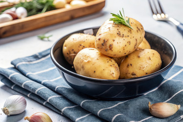 Свежесобранный картофель в миске на кухонном столе с зеленью. Генеративный ИИ - RomanZ