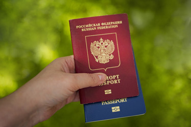 Рука держит два паспорта: один красный паспорт Российской Федерации и один синий. Размытый зеленый фон указывает на то, что действие происходит на открытом воздухе - Darya Petrenko