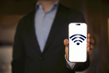 Бизнесмен в черном костюме держит смартфон с изображением символа Wi-Fi, размытый фон и теплое освещение создают профессиональную атмосферу для контента, связанного с технологиями - Darya Petrenko