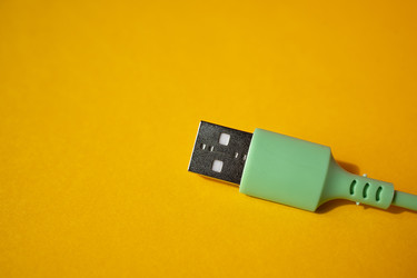 USB-кабель с зеленым разъемом и металлическим штекером на ярком желтом фоне, демонстрирующий детали конструкции разъема и кабеля - Darya Petrenko
