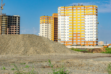 Склад гравия, готовый к дорожным или фундаментным работам в зоне городской застройки. На заднем плане видны башенный кран и недостроенное здание, выборочная фокусировка - dkorostilev78