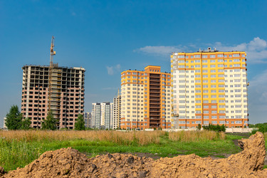 Башенный кран стоит рядом с железобетонным зданием, а на фотографии видны фасады готовых квартир. На переднем плане видны земляные насыпи и растительность - dkorostilev78