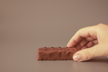 Рука, тянущаяся за шоколадным батончиком, на сером фоне - Gannachka