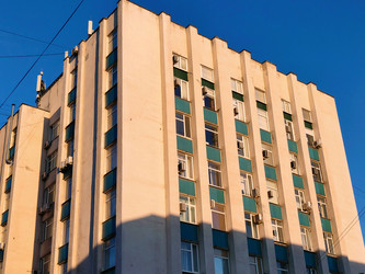 Многоэтажный жилой дом советской постройки: строгие вертикали пилонов, ряды окон с зелеными козырьками, кондиционеры на фасаде. Ракурс снизу, яркое синее небо, контрастные тени - DaniilAlexiy