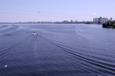 Поверхность воды в легкой ряби. Моторные лодки на воде. Левый берег с мостом на горизонте и летящие птицы.Россия Воронеж Июнь 13 2026 г - VitalySh