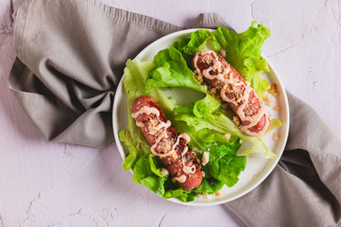 Крупный план жареной колбаски с соусом и гренками на листьях салата на тарелке, вид со стола - Elena Rui