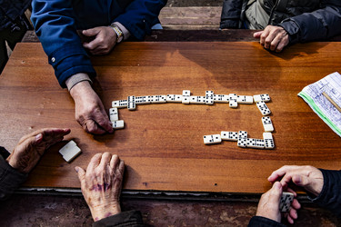 Пожилые люди играют в домино за деревянным столом на улице - Xandery