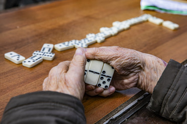 Пожилые люди играют в домино за деревянным столом на улице - Xandery