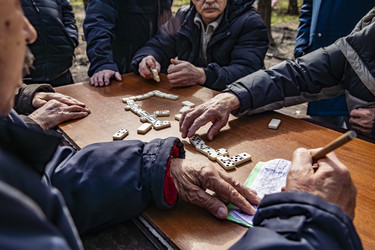 Пожилые люди играют в домино за деревянным столом на улице - Xandery
