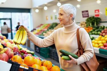 Женщина средних лет выбирает свежие продукты для здорового питания во время покупок в продуктовом магазине. - SeventyFour