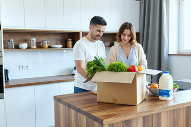 Взрослая пара распаковывает доставленные продукты на домашней кухне. - SeventyFour