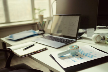 На рабочем столе размещены отчеты по бизнес-аналитике и ноутбук. - DragonImagesAsia