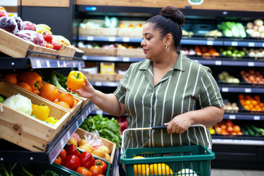 Взрослая женщина латиноамериканского происхождения выбирает свежие продукты для похода в продуктовый магазин. - SeventyFour