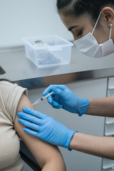 Взрослая женщина, получающая инъекцию вакцины во время посещения врача - AnnaStills