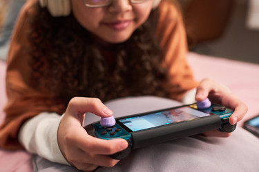 Азиатская девочка-подросток играет дома на портативной игровой консоли - Pressmaster