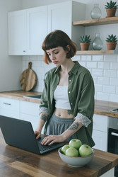 Взрослая женщина, работающая за ноутбуком на кухне для удаленной работы - SeventyFour