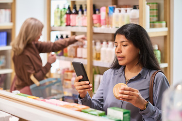 Испаноязычная женщина сканирует косметический продукт на смартфоне в магазине красоты - Pressmaster