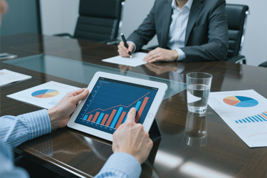 Бизнесмен просматривает аналитику продаж на планшете во время совещания - Pressmaster
