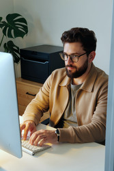 Взрослый мужчина работает за настольным компьютером в домашнем офисе. - Mediaphotos