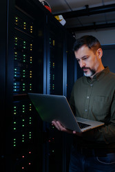 Мужчина средних лет контролирует серверную сеть с помощью ноутбука - DragonImagesAsia