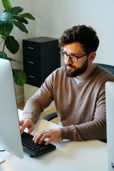 Взрослый мужчина работает за настольным компьютером в современном офисе. - Mediaphotos