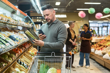 Мужчина сравнивает информацию о продуктовом продукте на смартфоне в супермаркете - Pressmaster