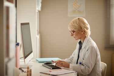 Женщина-педиатр средних лет просматривает записи пациентов - SeventyFour