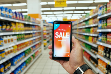 Взрослый держит в руке смартфон, демонстрирующий акцию по продаже в супермаркете - DragonImagesAsia