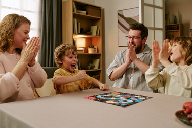 Родители и дети аплодируют во время домашней настольной игры family time - AnnaStills