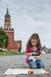 Маленькая девочка в нарядном платье сидит на сетке возле Кремля и рассматривает карту в лупе - paha_l