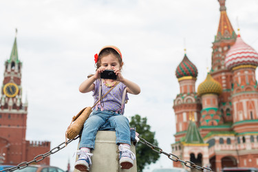 Маленькая девочка в джинсах и кепке возле Кремля сидит на бетоне и фотографирует на фотоаппарат - paha_l