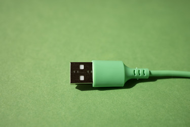 Зеленый USB-разъем с прямоугольным металлическим наконечником на сплошном зеленом фоне, демонстрирующий крупным планом зарядное устройство - Darya Petrenko