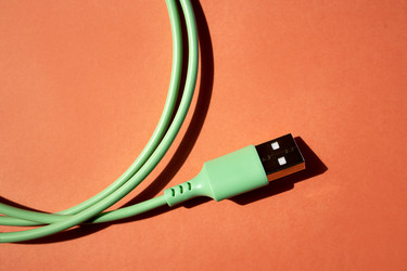 Зеленый USB-кабель с прямоугольным разъемом на оранжевом фоне, демонстрирующий текстуру и детали дизайна кабеля для контента, связанного с технологиями - Darya Petrenko