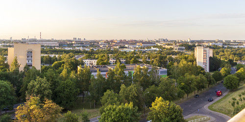 Панорамный вид сверху на зеленый пригородный жилой район с многоквартирными домами, густыми деревьями и городским пейзажем на закате. Пейзаж - Pazemin