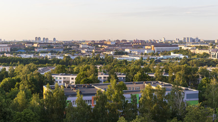 Панорамный вид сверху на зеленый пригородный жилой район с многоквартирными домами, густыми деревьями и городским пейзажем на закате. Пейзаж - Pazemin