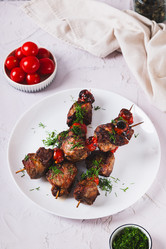 Жареное мясо, запеченное со специями, с помидорами черри на шампурах, на тарелке на столе (вертикальный вид) - Elena Rui