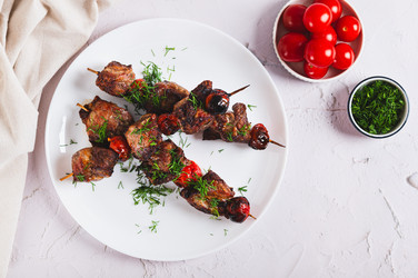 Вкусный кебаб на шампурах с помидорами, приготовленный во фритюрнице, на тарелке, вид со стола - Elena Rui
