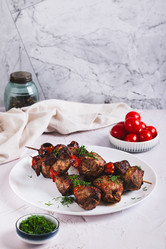 Вкусный кебаб на шампурах с помидорами, приготовленный во фритюрнице, на тарелке на столе (вертикальный вид) - Elena Rui