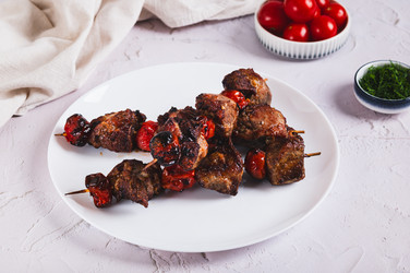 Жареное мясо, запеченное в специях, с помидорами черри на шампурах, подается на тарелке на столе - Elena Rui