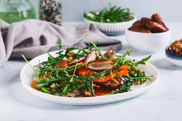 Вегетарианский салат с финиками, морковью, рукколой и орехами на тарелке на столе - Elena Rui