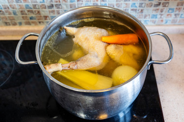 Куриный бульон, кипящий с овощами в стальной кастрюле - vale